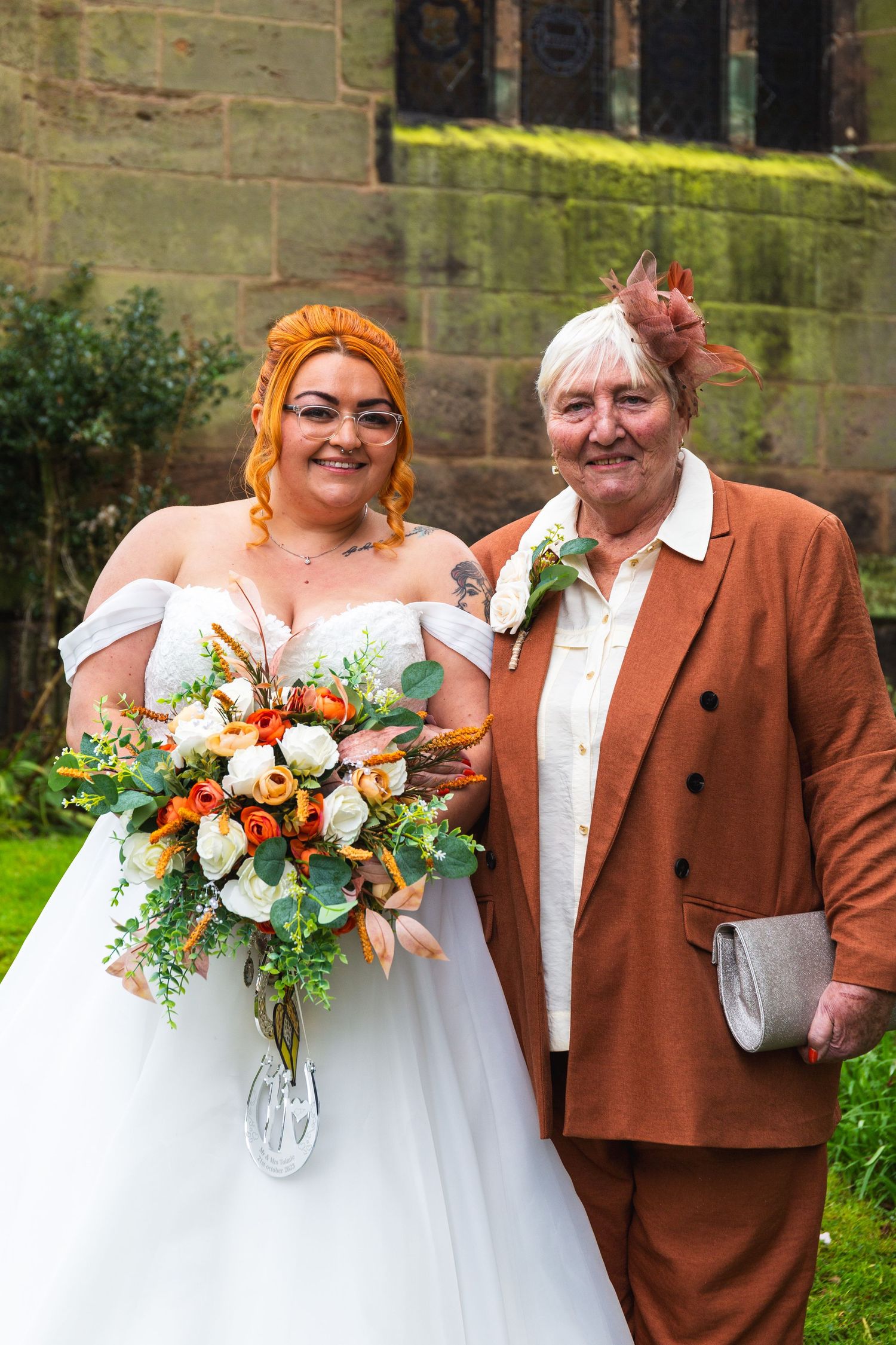 A bride with bright hair holds a colorful bouquet while standing next to someone in a rust-colored suit.