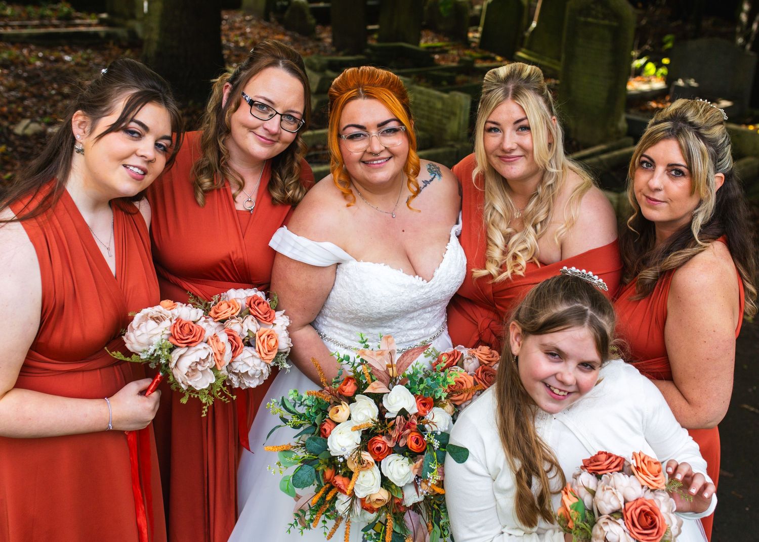 Wedding party in coral red dresses posing together with bouquets of white and peach flowers.