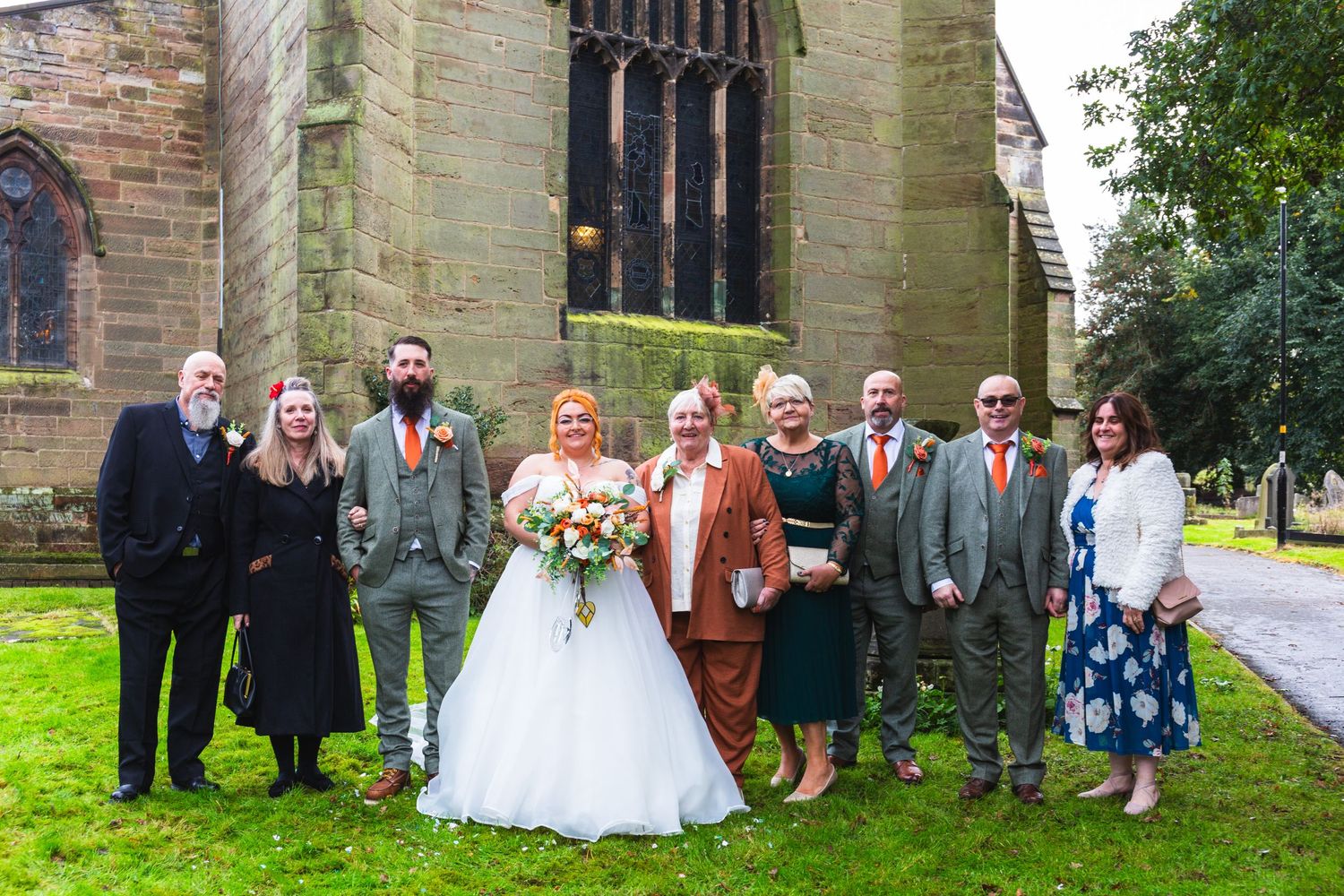 Wedding party members pose together outside a historic stone church building.