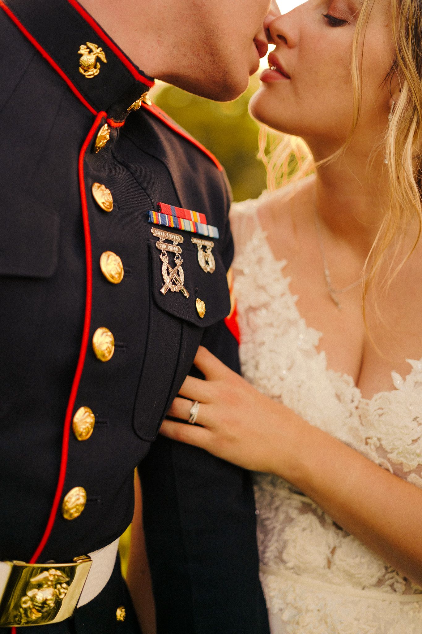 Close-up details of a military dress uniform and white lace wedding dress during an intimate moment.