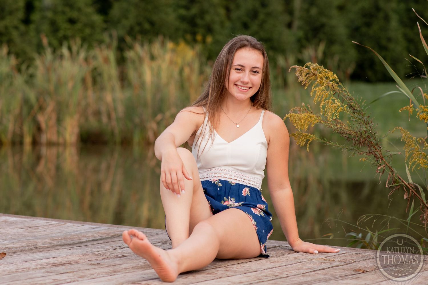 A summer portrait shot on a wooden dock with a serene lake and cattails in the background.