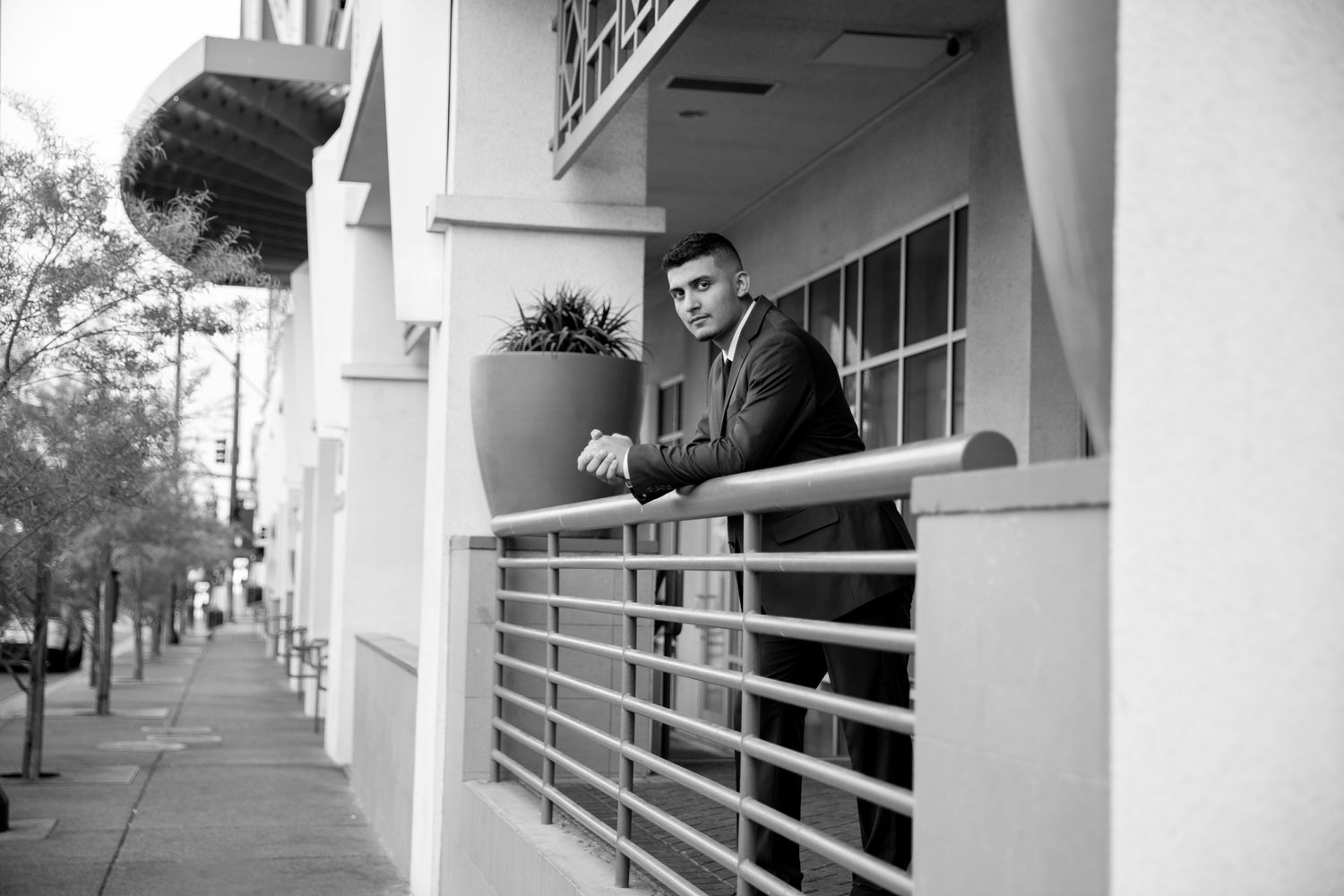Black and white photo of a well-dressed person standing on an urban balcony with metal railing.