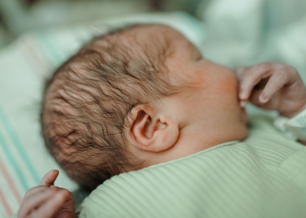 Details of a newborn baby wearing a green sleeper, sleeping in his bassinet.