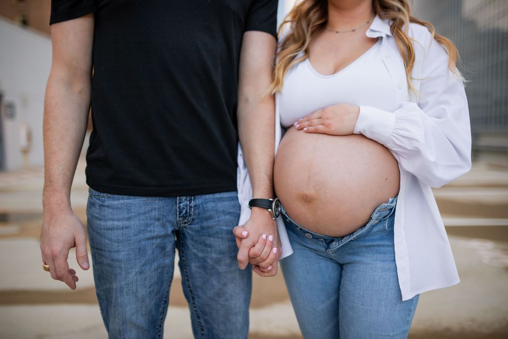 A maternity session with a couple posing in denim jeans and white button down.
