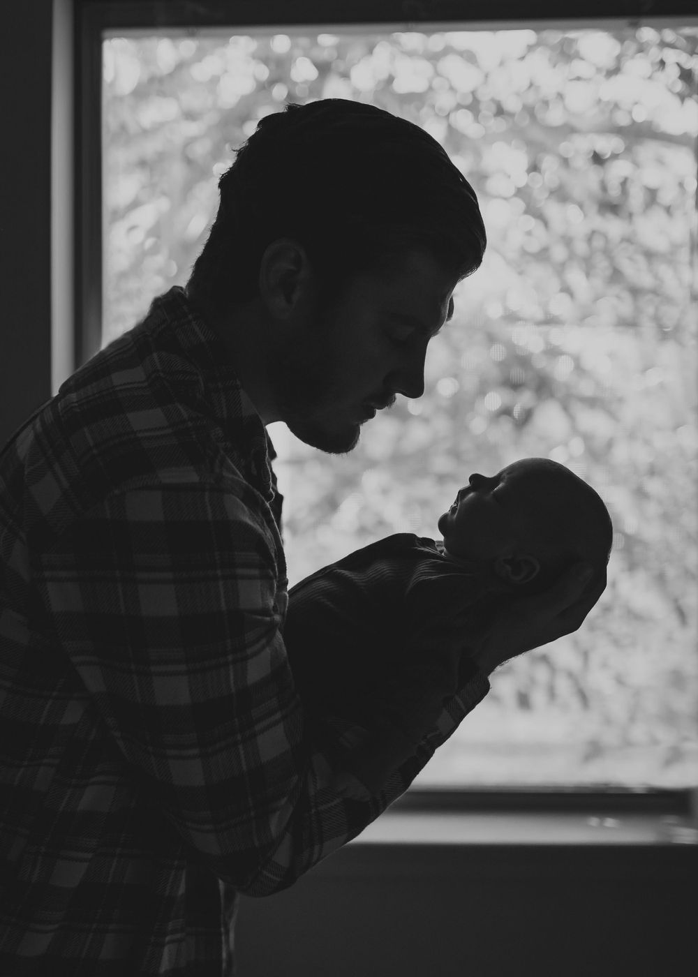 A silhouetted figure of a father and baby in profile view posing for a photo during their newborn session.