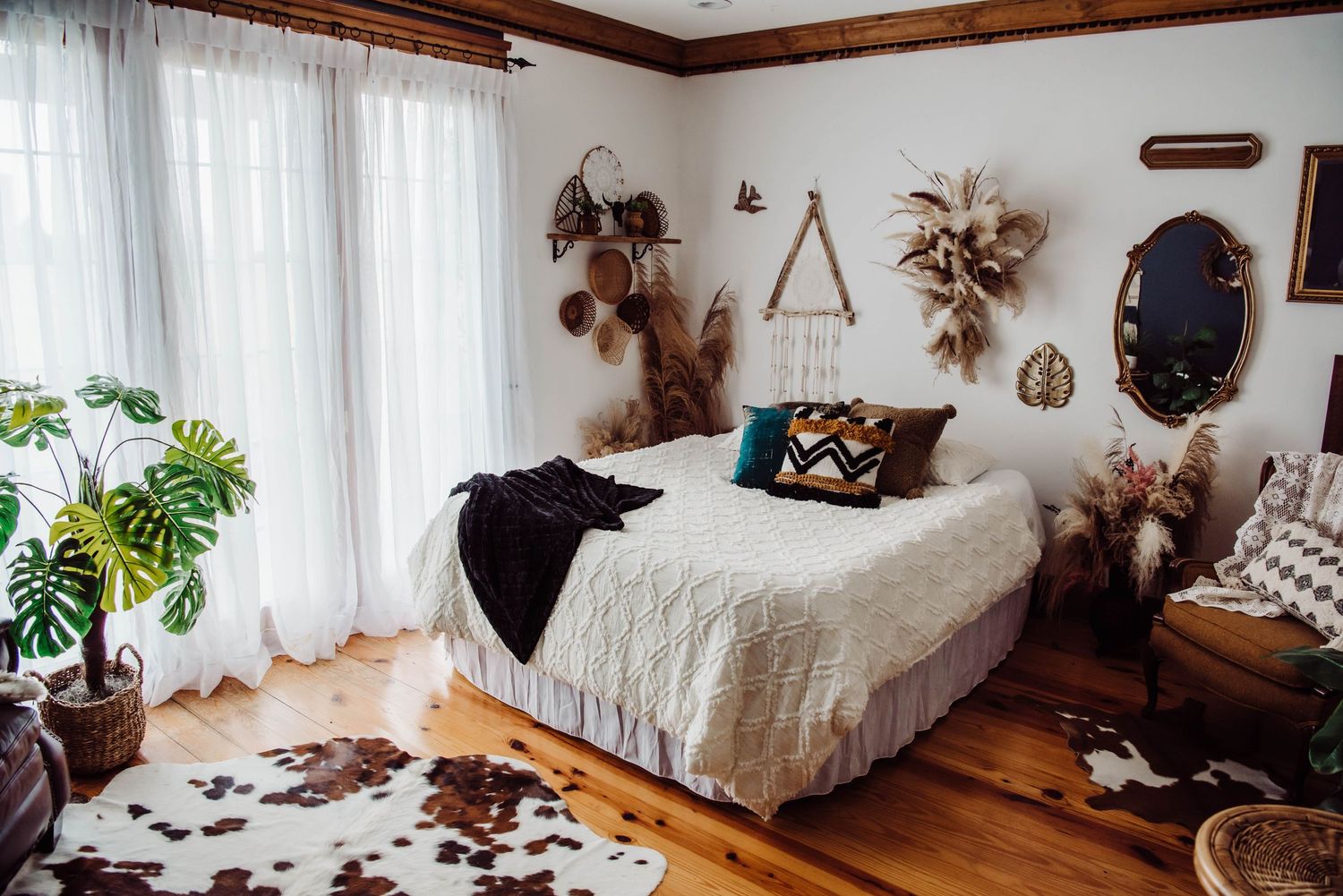 A cozy boho bedroom with white bedding, plants, and natural decor on rustic wooden floors.