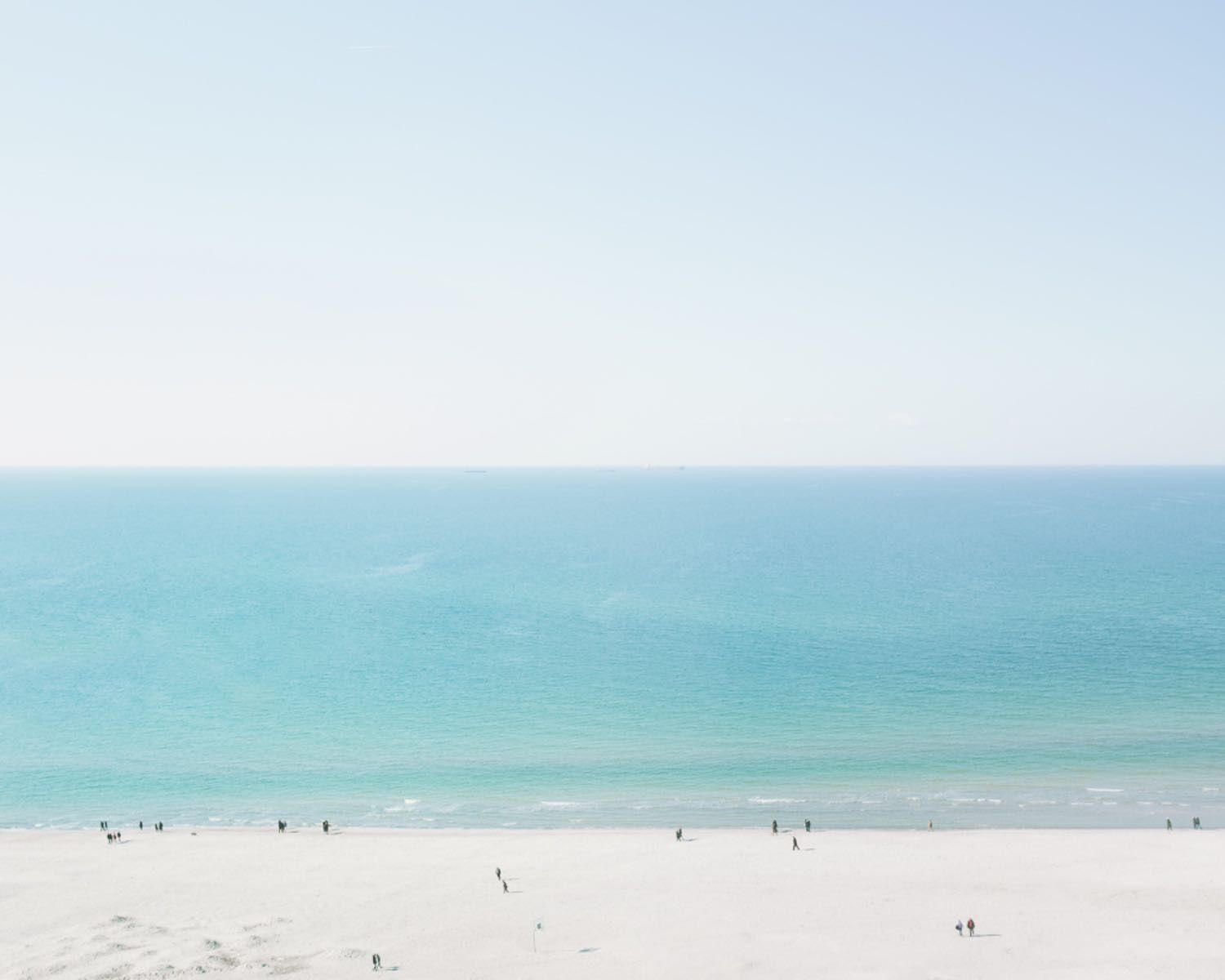Minimalist beach scene with turquoise water and tiny beachgoers dotting the white sandy shore.