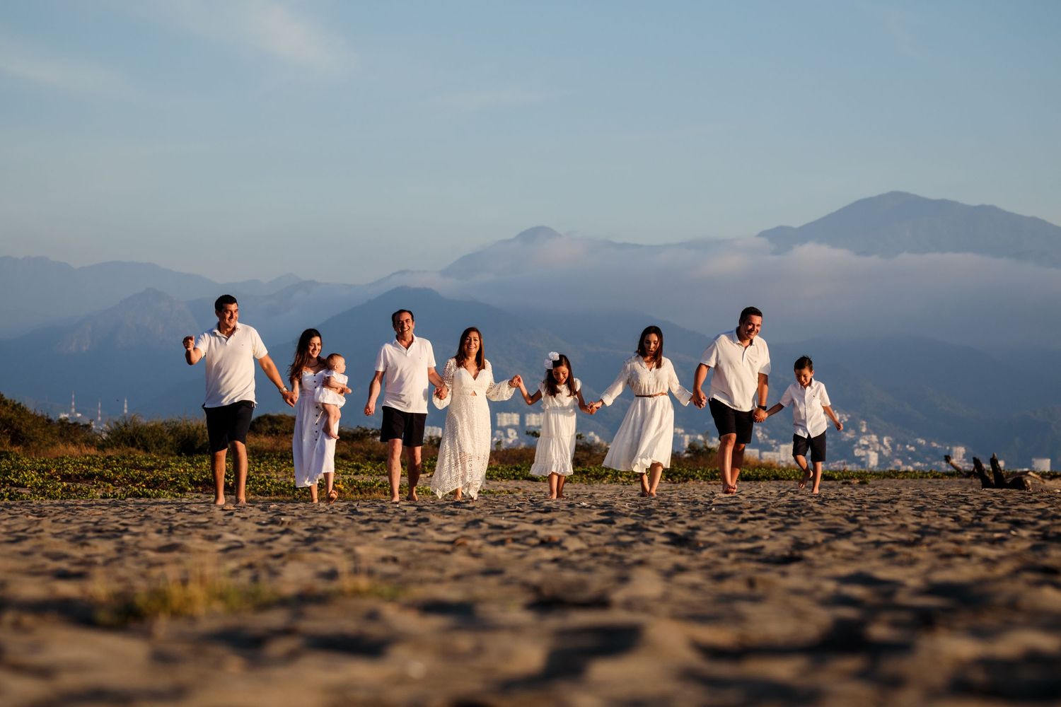 Group walking together on a beach at sunset with mountains in the background wearing white clothing.