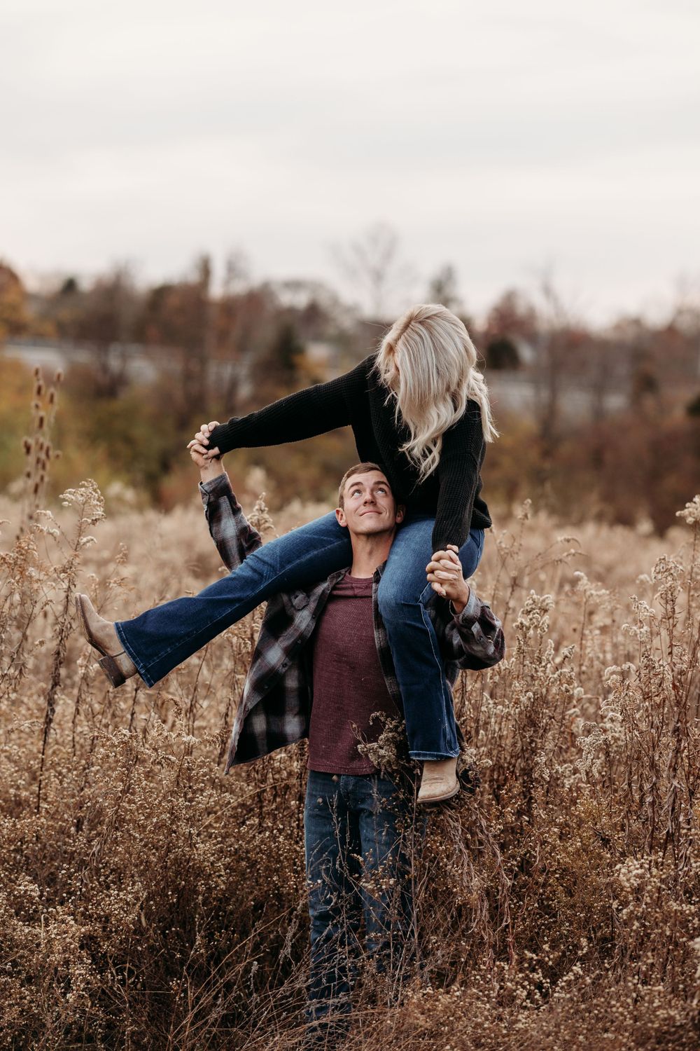 Couple having fun with piggyback ride in tall grass during golden hour.