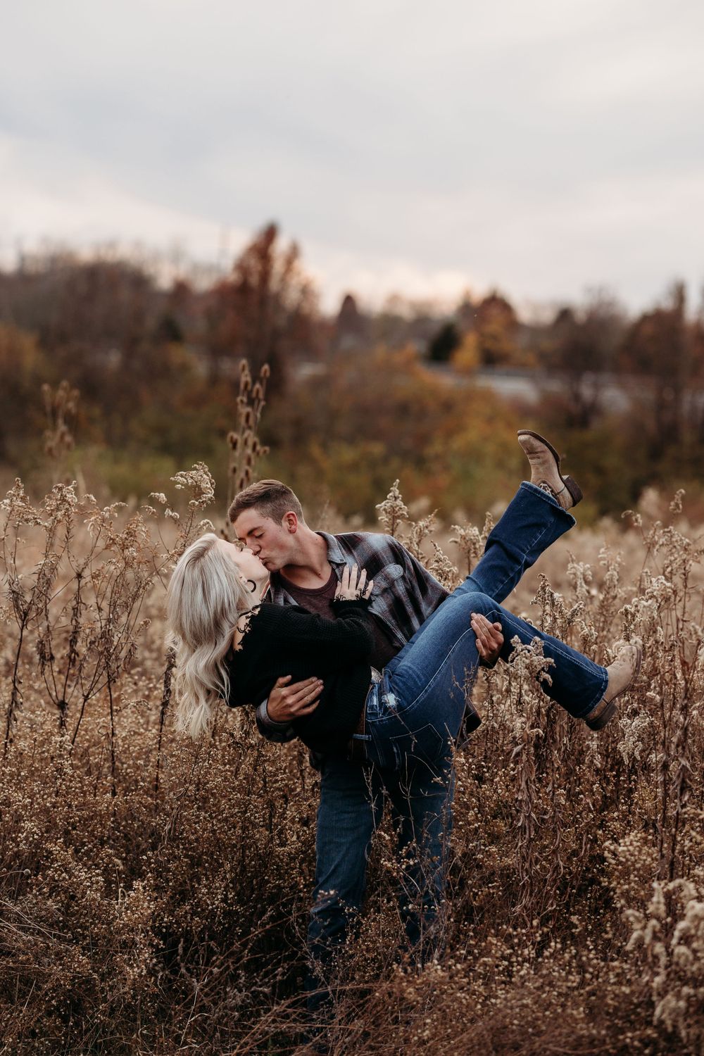 Romantic dip pose amid autumn wildflowers during couple's photoshoot.