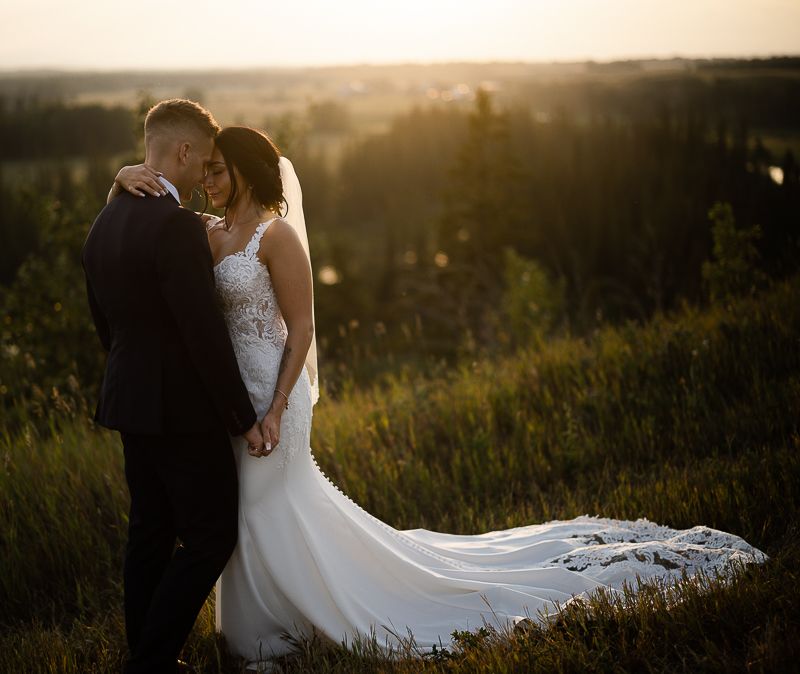 A bride's flowing white dress trails behind as couple shares intimate moment at sunset.