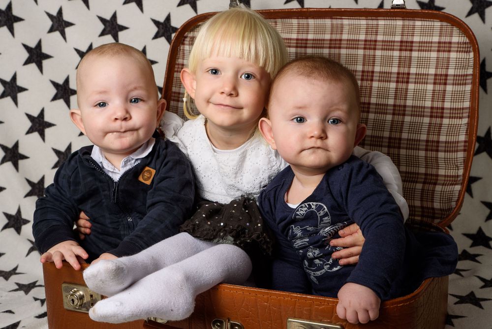 Three young children including two babies and a toddler sitting together in a vintage suitcase.