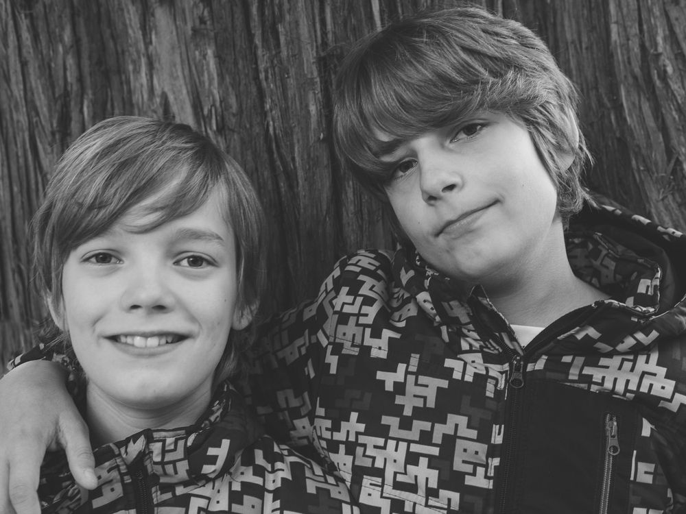 Black and white close-up portrait of two smiling boys with shaggy hair leaning together outdoors.