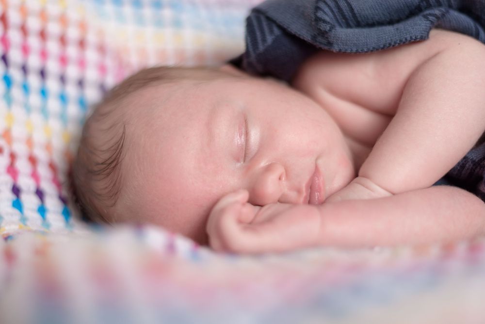 Peaceful newborn baby sleeping on a colorful blanket with cheek resting on tiny hands.