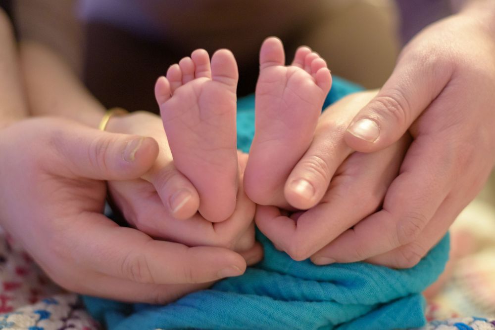 Newborn baby tiny feet cradled gently in two adult hands on a blue blanket.