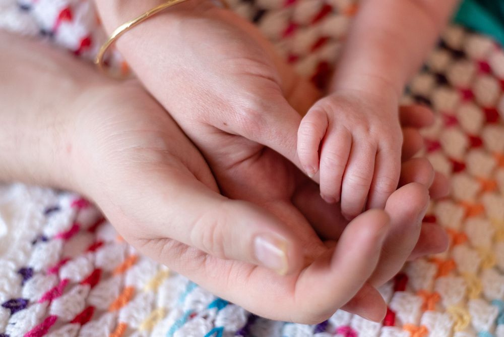 Newborn baby hand gently clasping an adult finger on a colorful crocheted blanket.