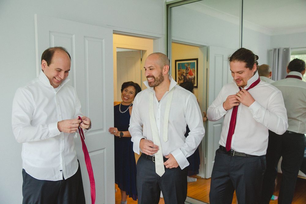 Groomsmen help each other prepare by adjusting their ties and formal attire.