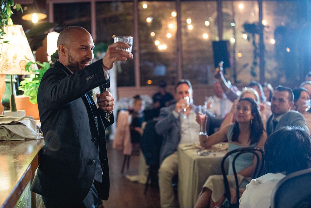 Indoor wedding celebration with guests gathered in a warmly lit venue with exposed brick walls.