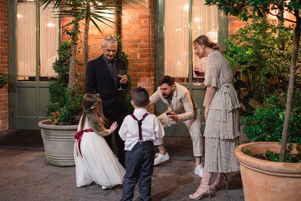 Wedding ceremony taking place in an elegant indoor venue decorated with greenery and floral arrangements.