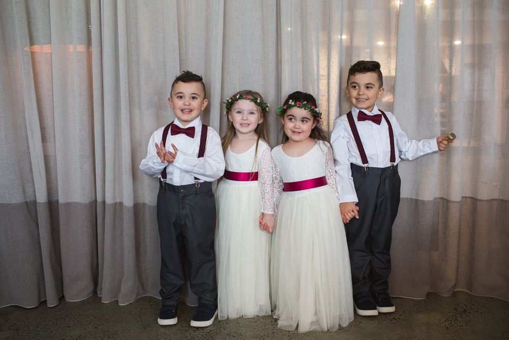Children in formal wedding attire posing against a curtained backdrop.