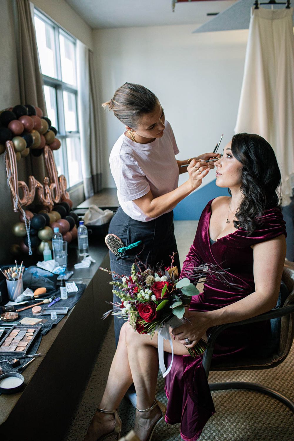 Wedding preparation scene with makeup application and burgundy velvet dress details.
