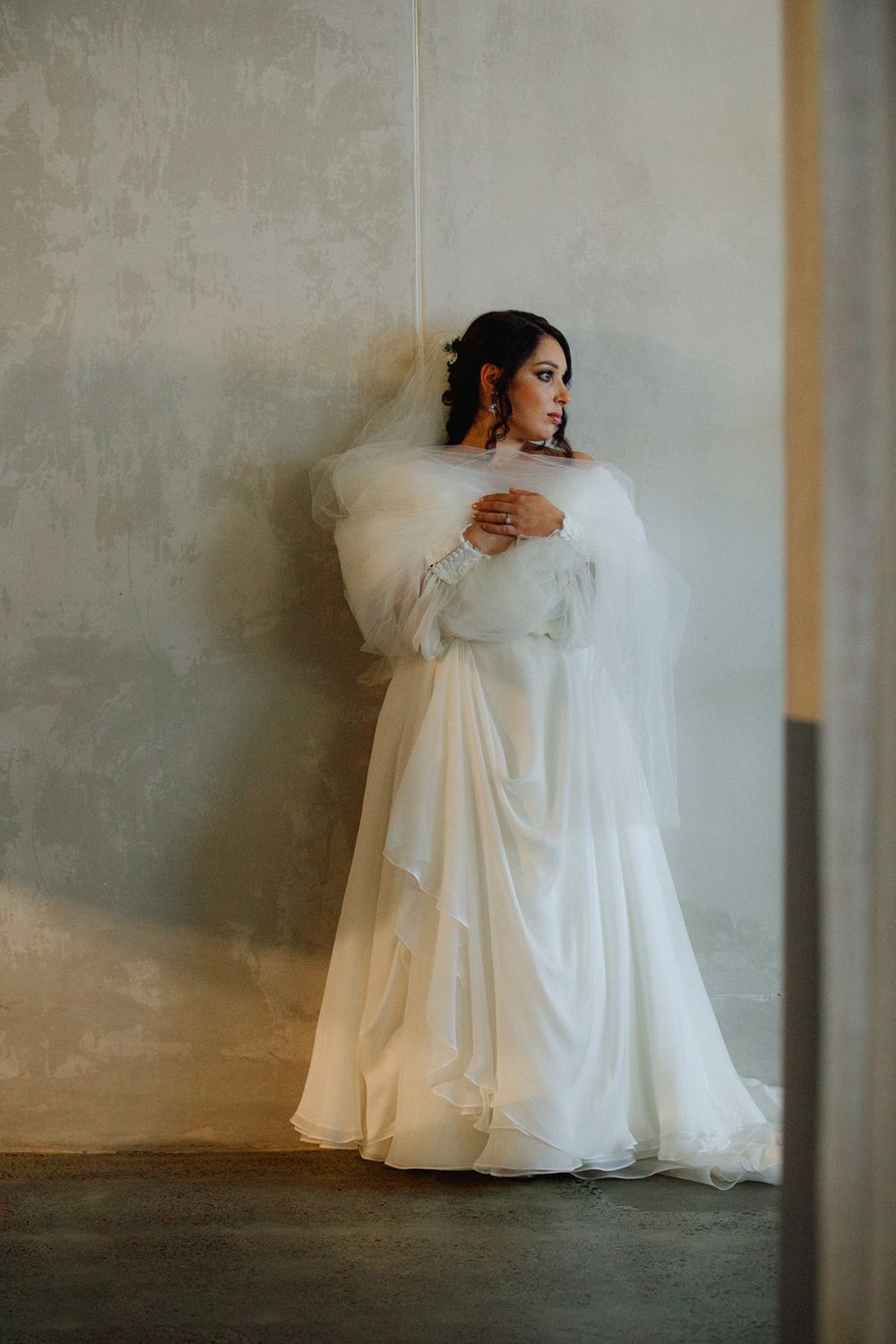 Artistic bridal portraits against a textured grey wall showing movement in the wedding dress.