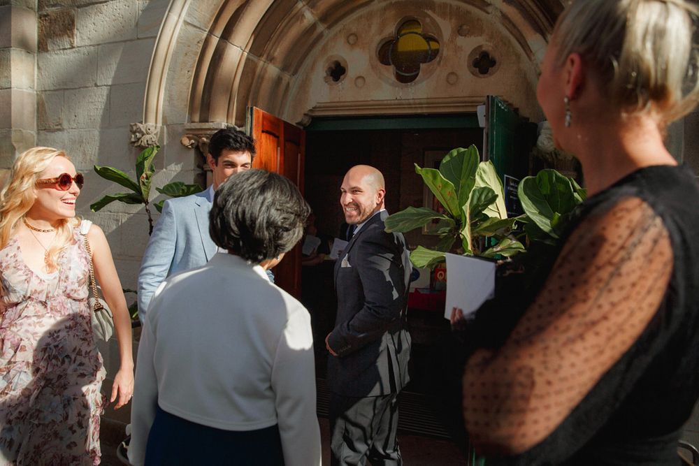 Wedding guests mingling in an ornate church entrance with arched doorways.