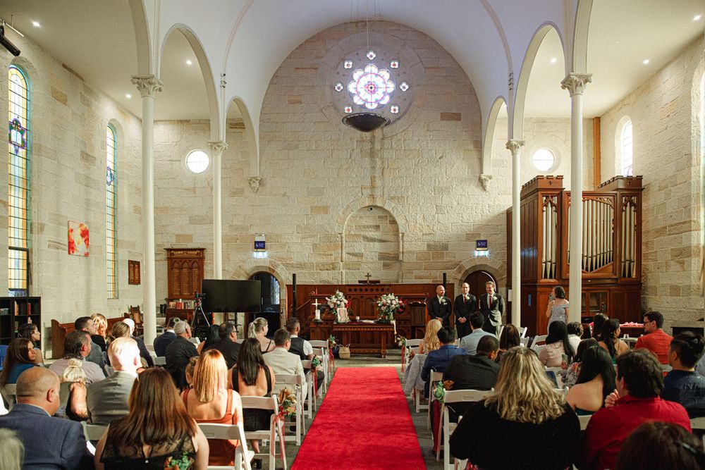 Interior of a church with vaulted ceilings, red carpet, and white stone walls during a ceremony.