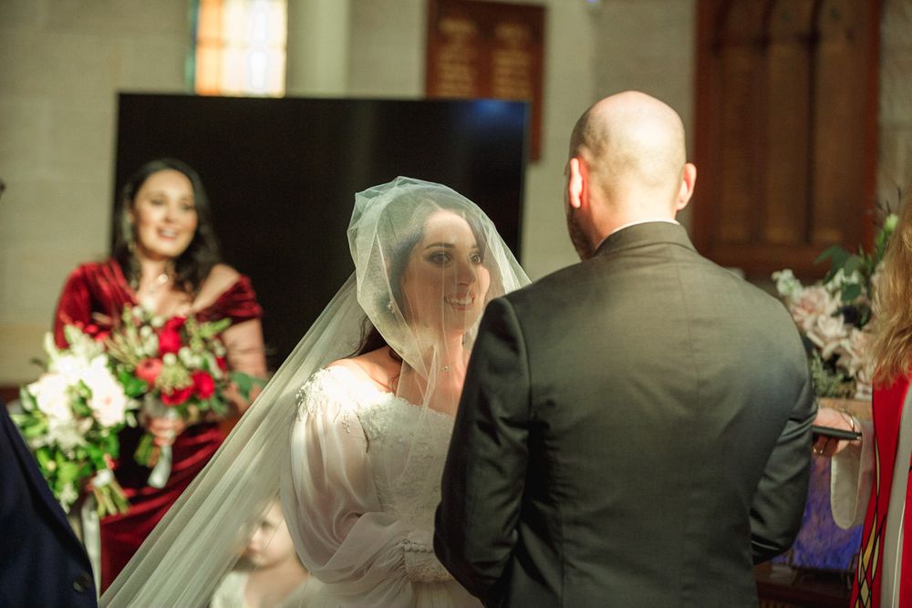 Wedding ceremony participants standing at the front of a church with floral decorations.