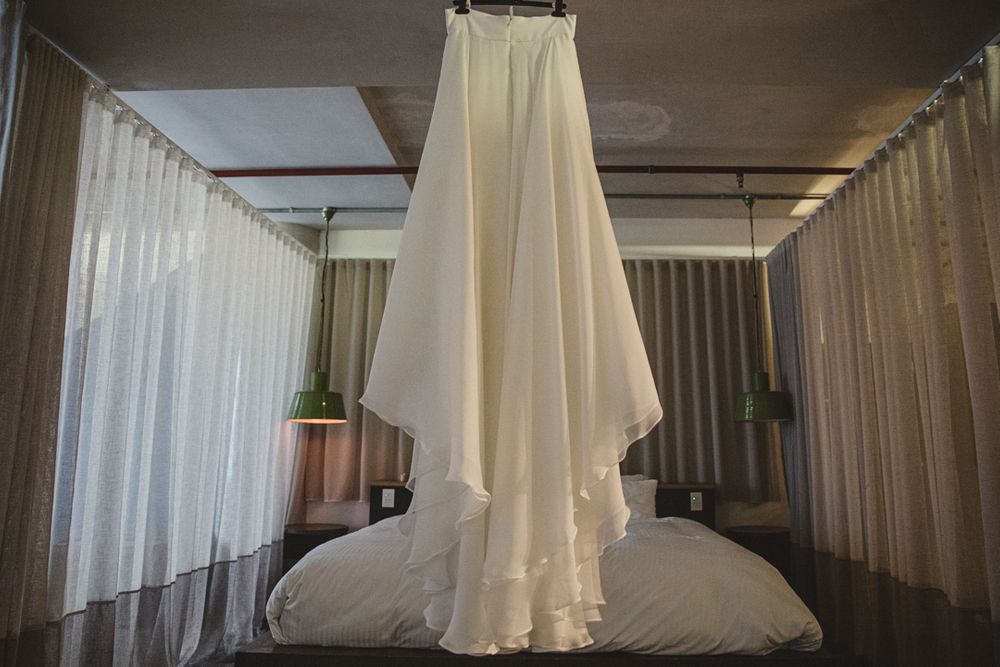 White wedding dress hangs elegantly in a room with flowing curtains and natural light.