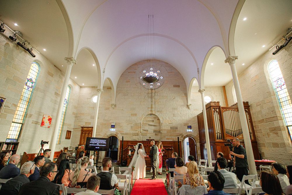 Panoramic shot of a church interior with white arched ceilings and religious artwork.