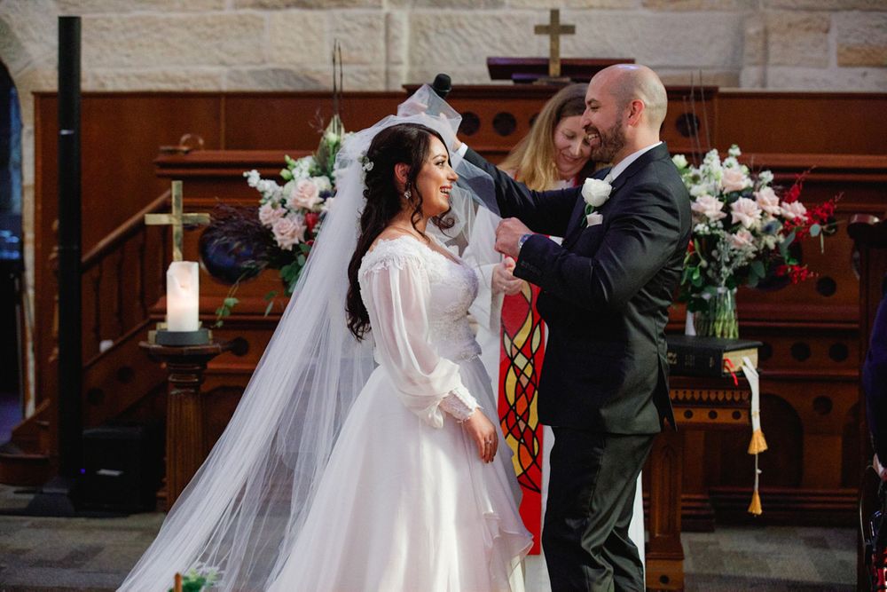 Wedding ceremony taking place in a traditional stone church with decorative floral arrangements.