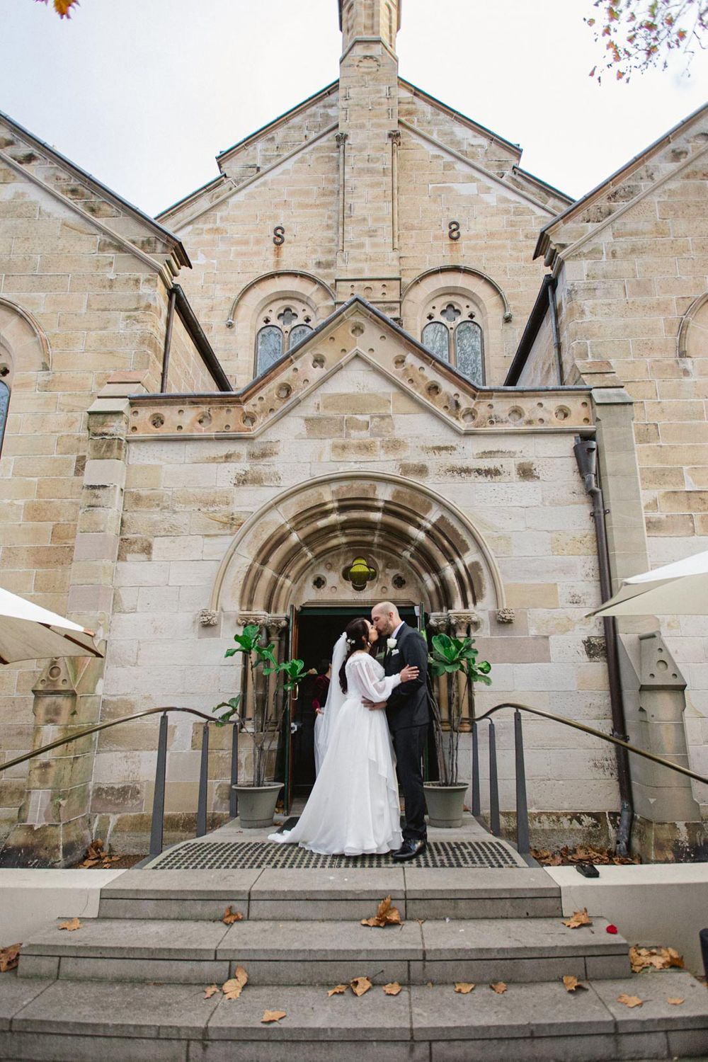 Gothic stone church exterior with ornate architecture serves as backdrop for wedding ceremony.