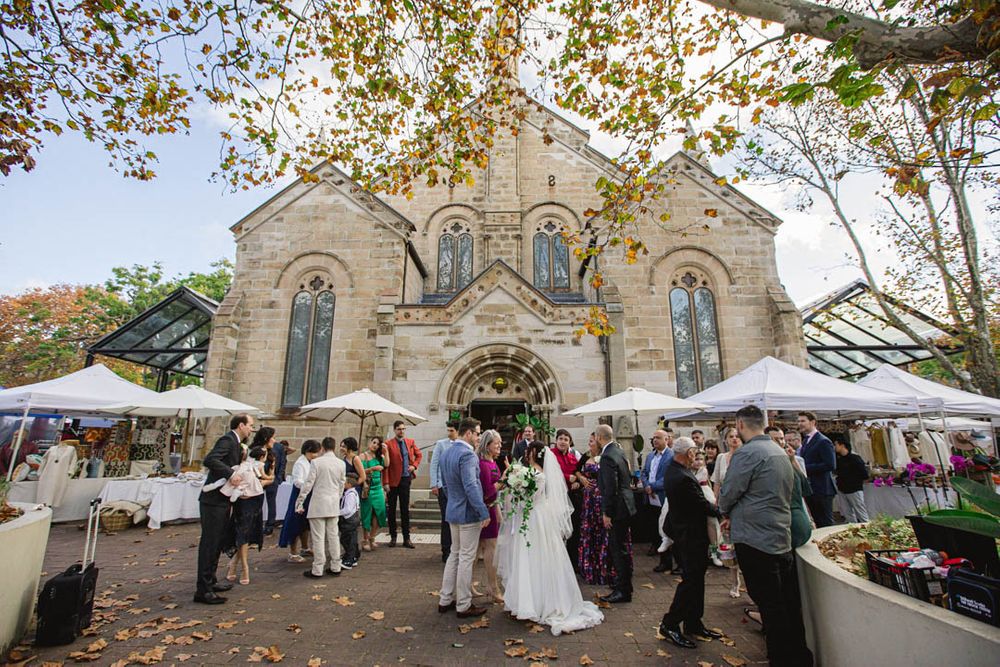 Wedding celebration outside historic church with autumn trees and white tent setup.