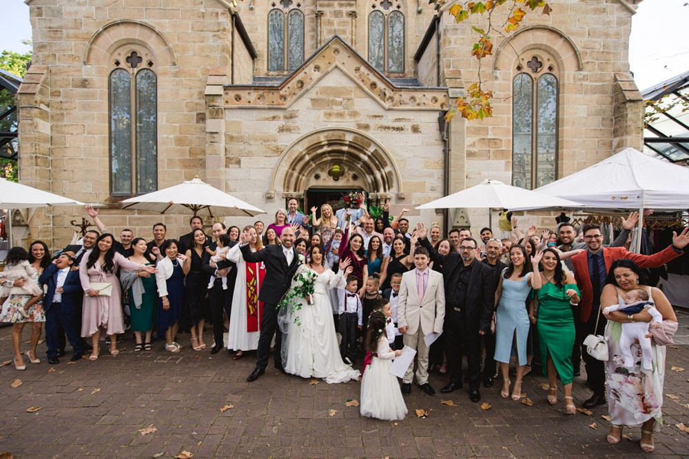 Wedding guests gather for group portrait outside historic church building.