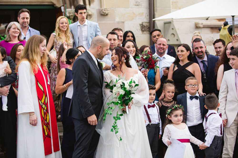 Wedding party and guests celebrate outside church with formal attire and decorations.