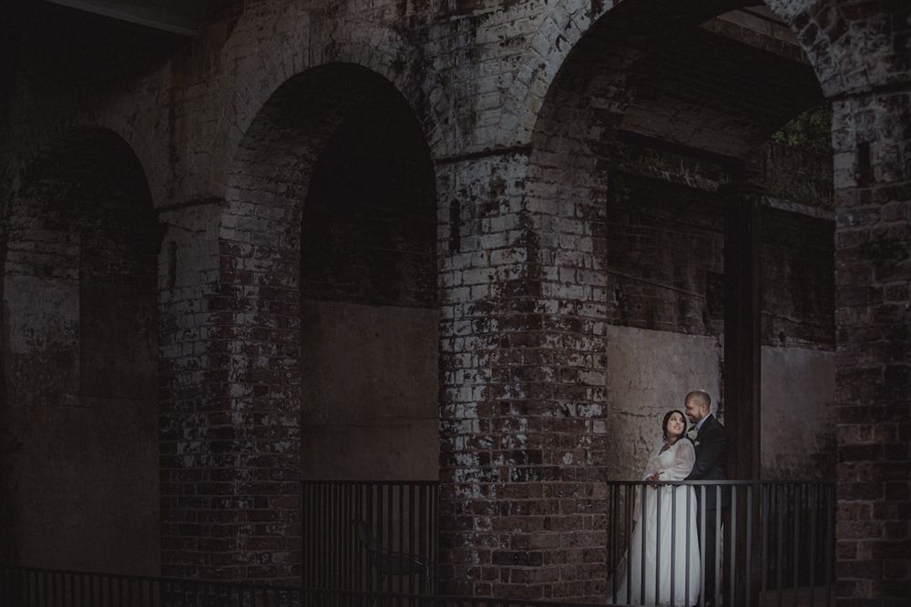 Dramatic black and white photo of couple in historic brick corridor.