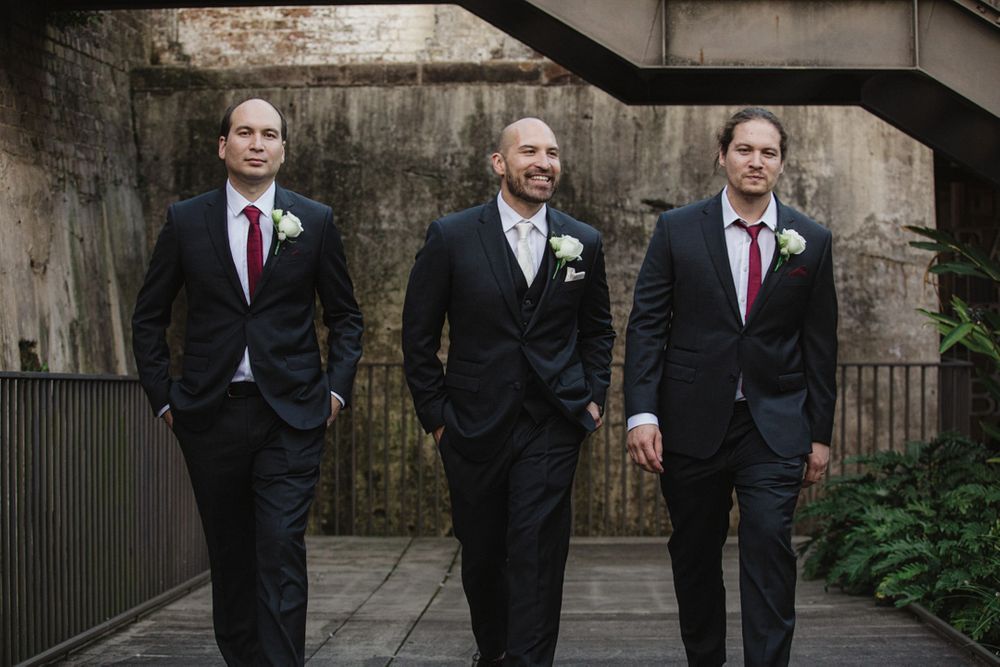 Wedding party members in formal attire arranged along historic brick corridor.