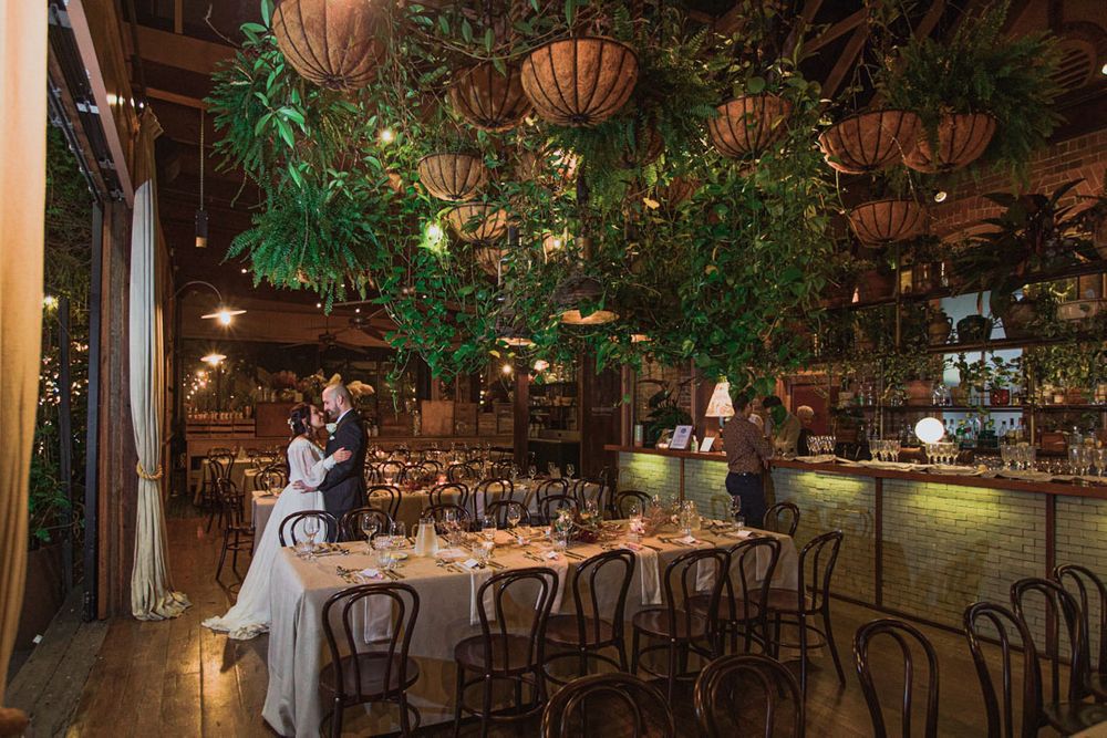 Elegant wedding reception venue decorated with warm lighting, hanging lanterns, and lush greenery.
