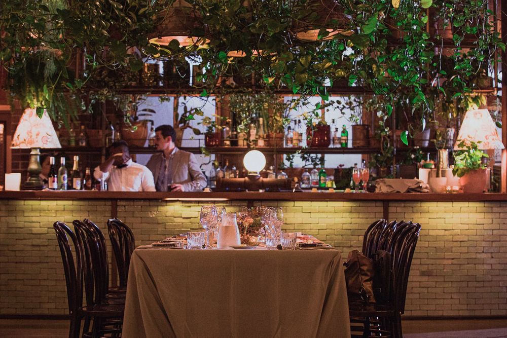 Wedding reception setup with elegant table settings, brick walls, and hanging greenery.