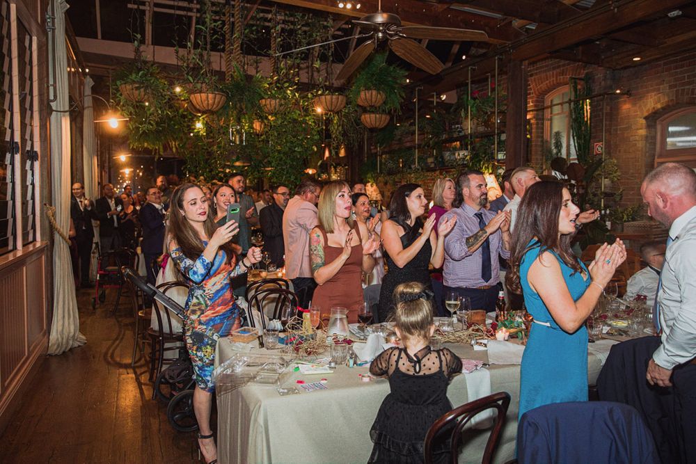 Wedding guests dancing and celebrating on a dimly lit dance floor.