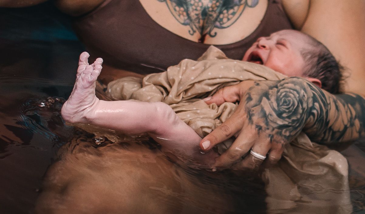 mother holds new baby in birthing pool at home birth