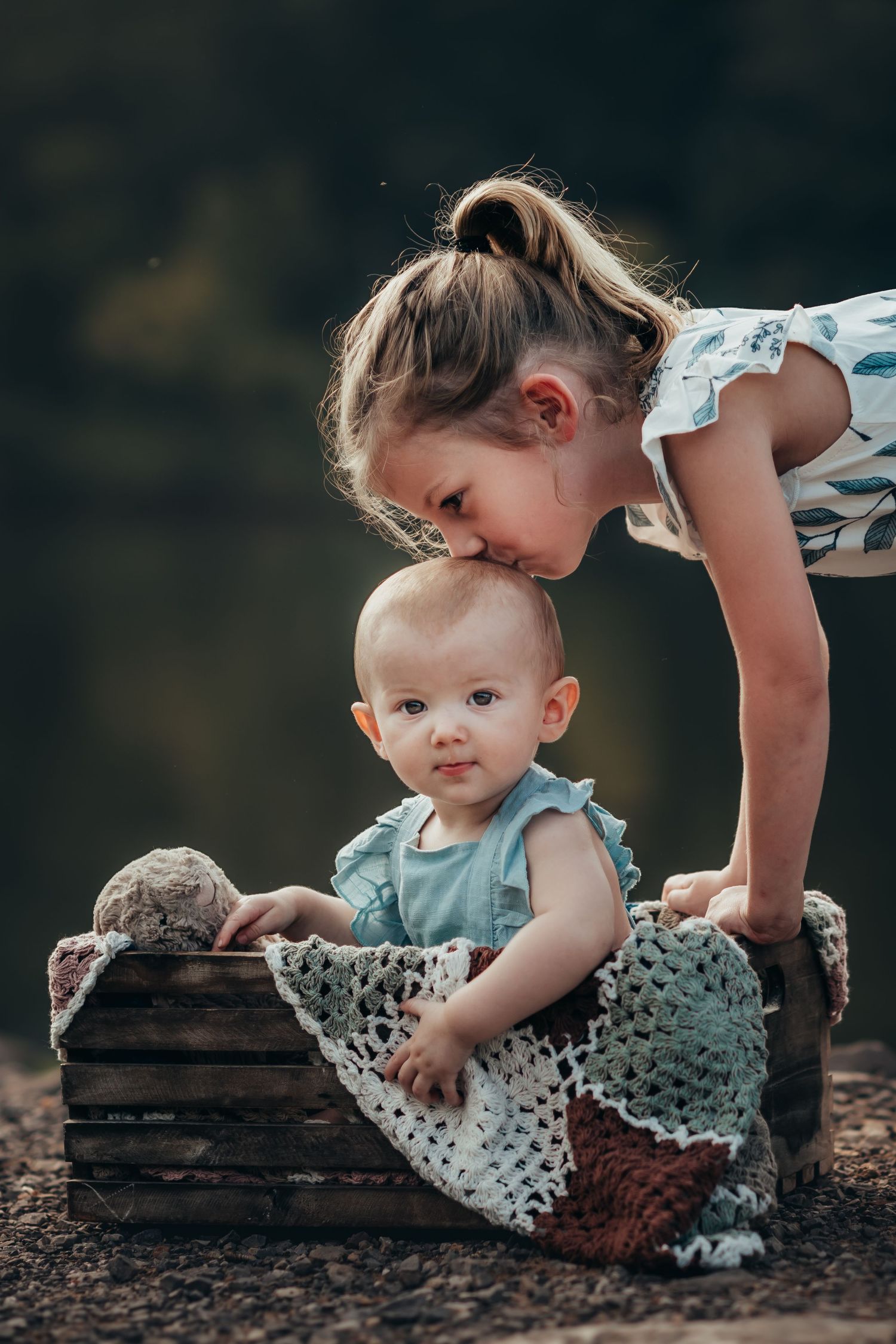 big sister bends over and kisses the top of little sister's head for family photos