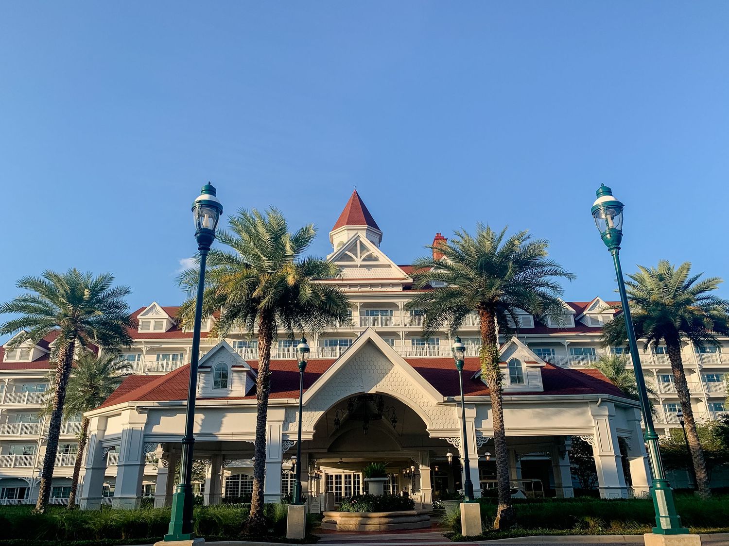 Victorian-style resort buildings with white facades and red roofs under blue sky with palm trees.