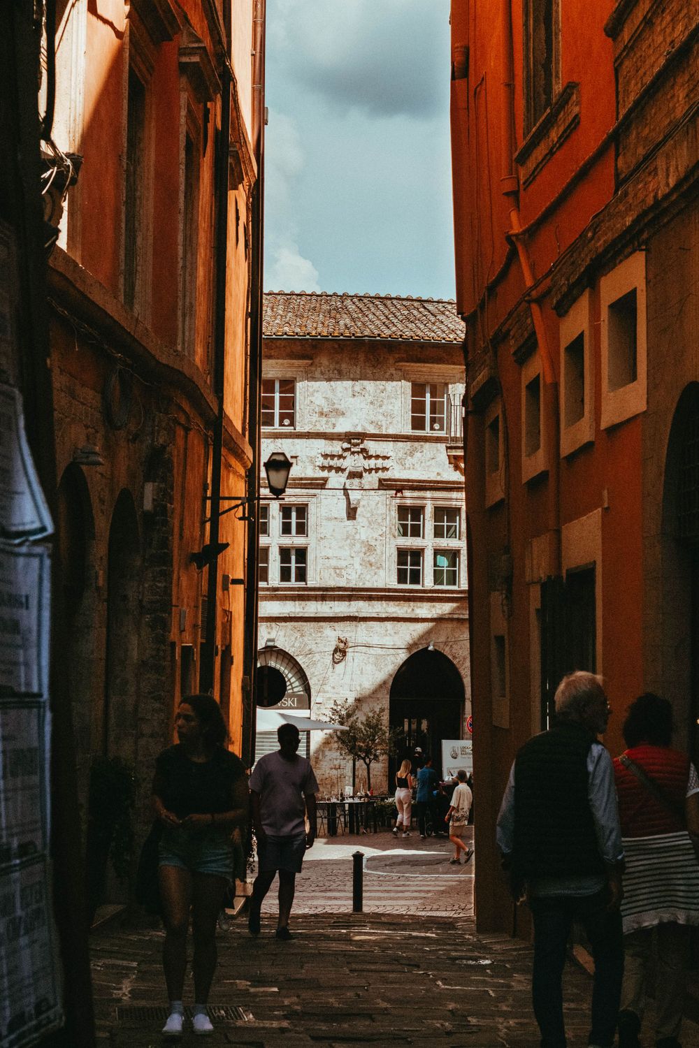 Narrow cobblestone alley between historic orange buildings leading to an archway in a European city.