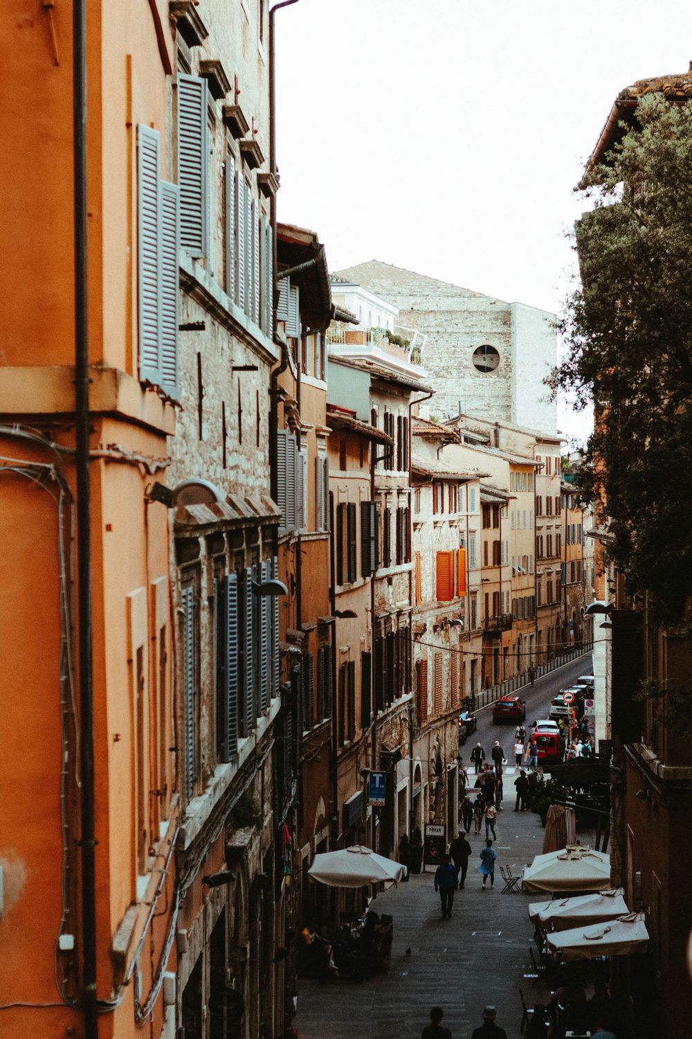 Steep narrow street in an Italian city with colorful buildings and pedestrians.