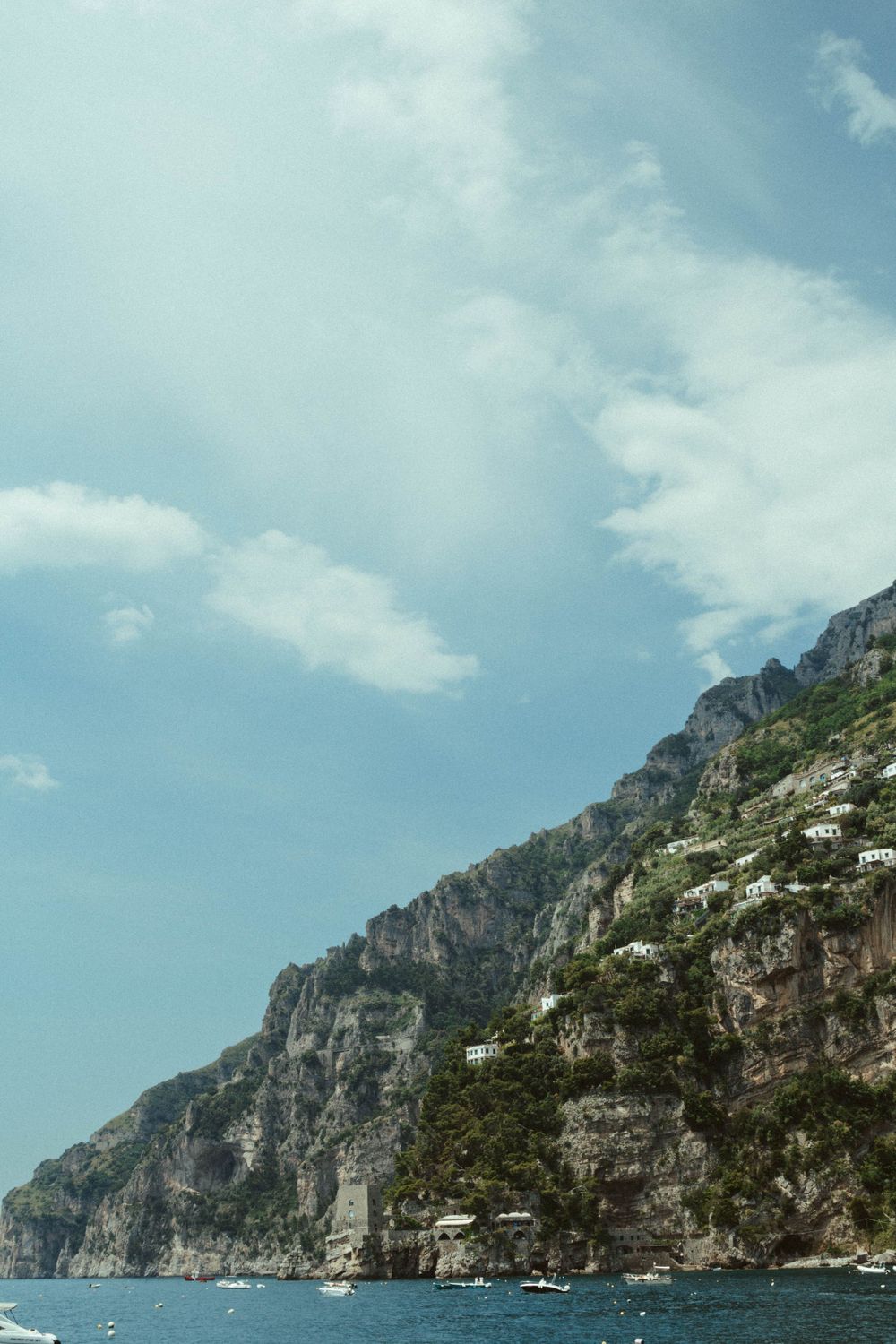 Dramatic rocky coastal cliffs rise above blue Mediterranean waters under a bright summer sky.