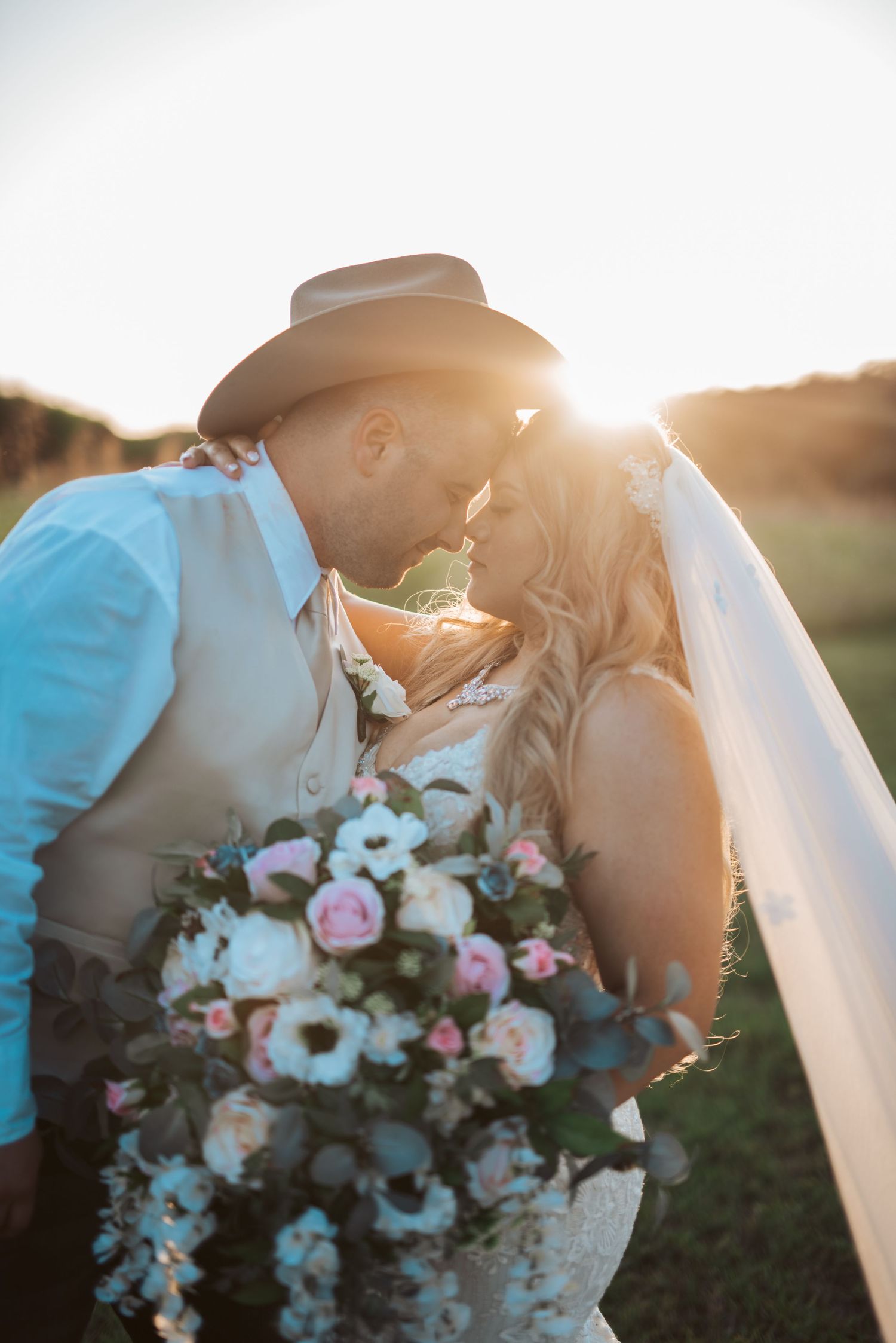 Romantic sunset portrait of couple with floral bouquet in cowboy hat and wedding attire.