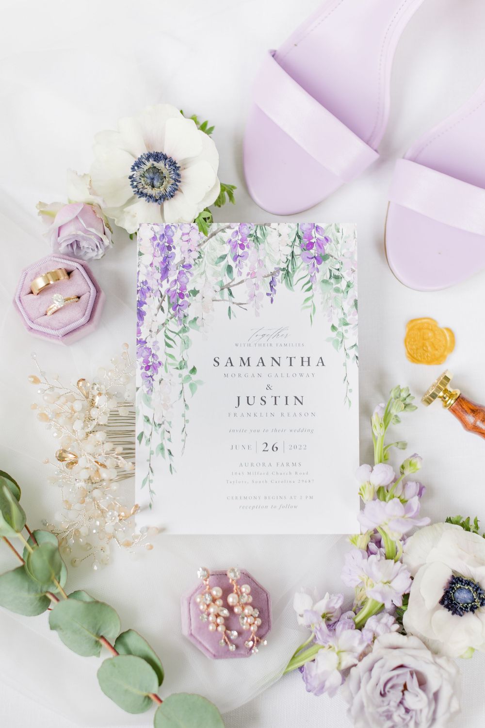 Wedding invitation with purple floral design surrounded by flowers and pink accessories.