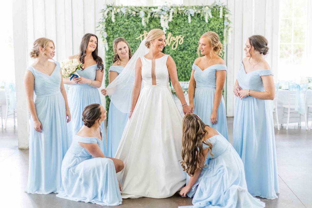 Bridal party in powder blue gowns gathering around bride in white wedding dress.